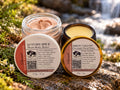 NOURISH gift bundle with Autumn Spice Bison Body Butter and Bison Tallow Overnight Facial Balm, with their labelled lids on mossy rock beside water