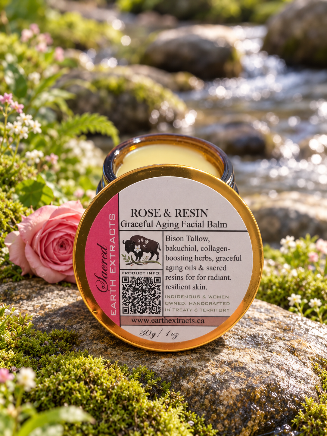 Rose & Resin Bison Facial Balm on mossy rocks beside flowing water, wildflowers and a pink rose.
