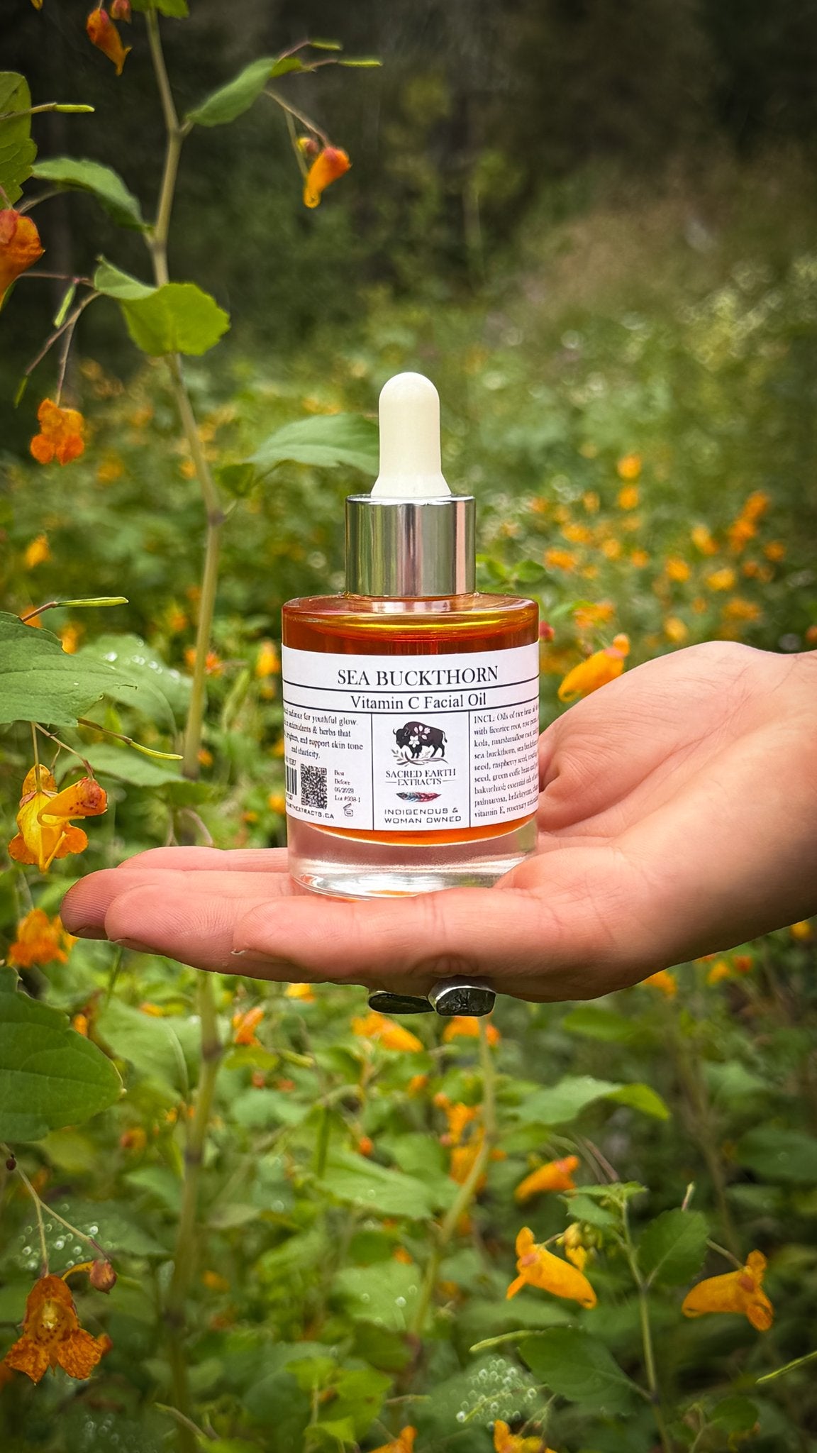 Sea Buckthorn Vitamin C facial oil held in an open hand among orange wildflowers