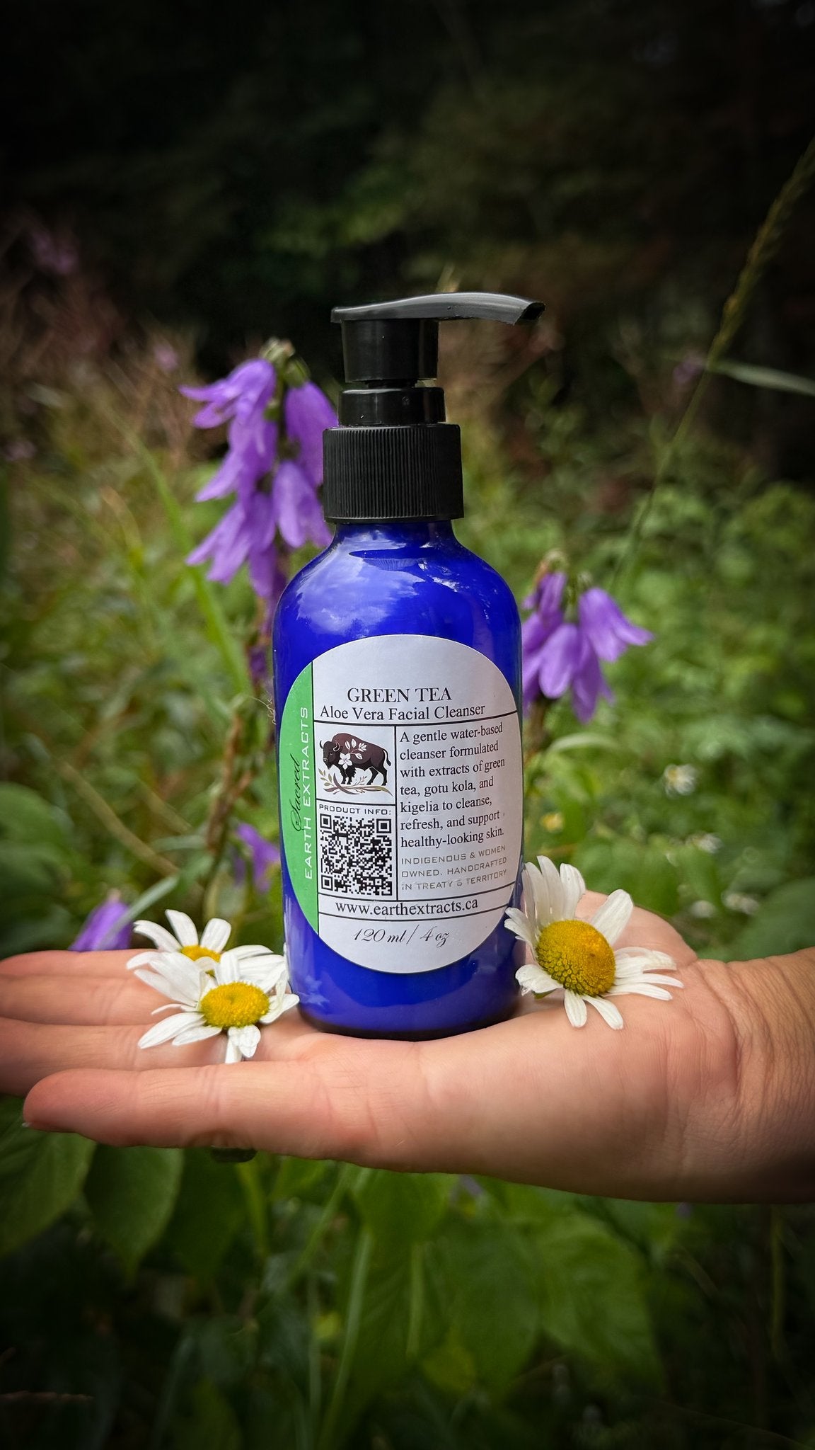 Green Tea Aloe Vera facial cleanser in a blue pump bottle held in an open hand with daisies